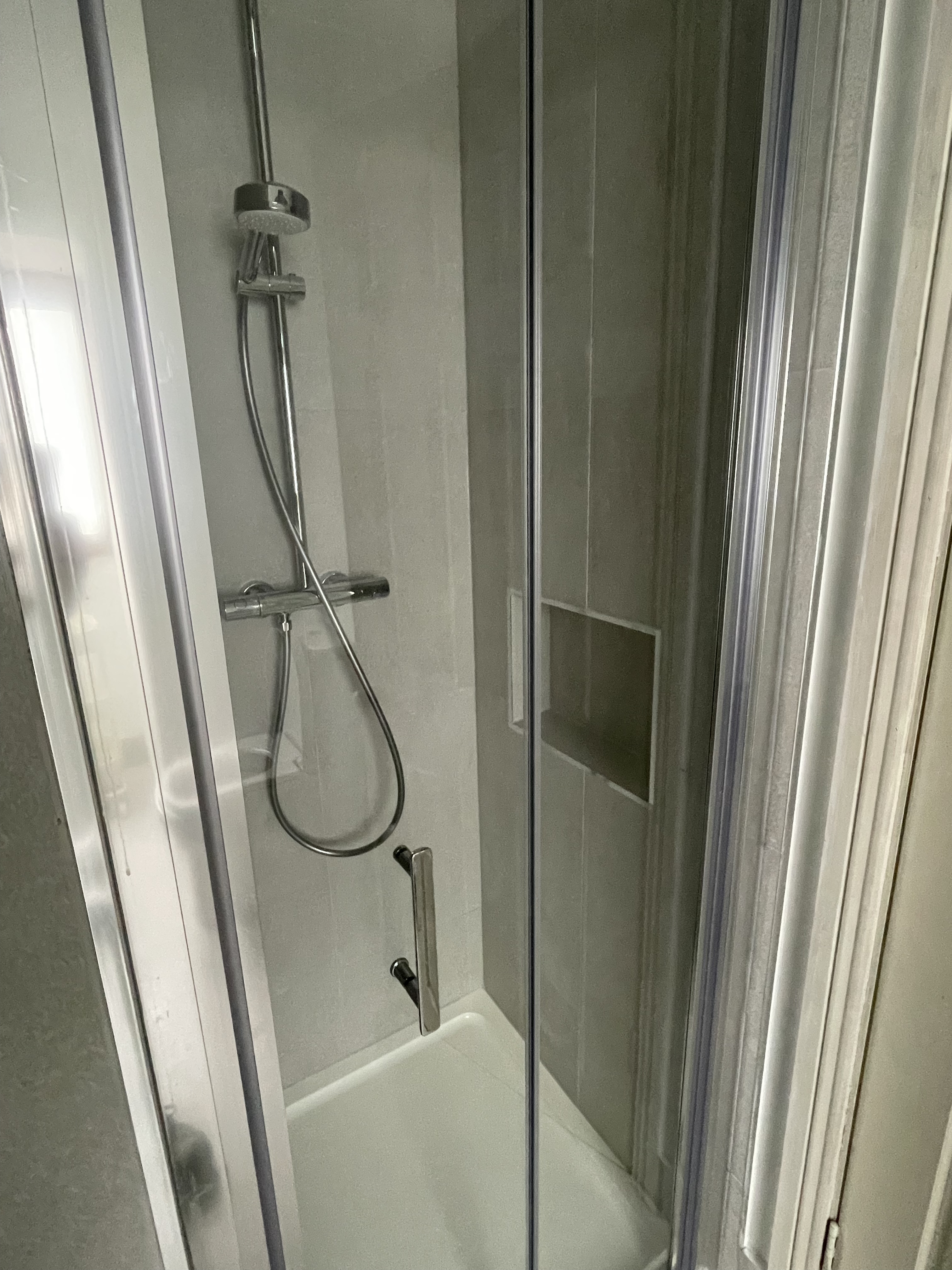 Close up of a shower with a cut in hole in the wall and stainless steel shower head