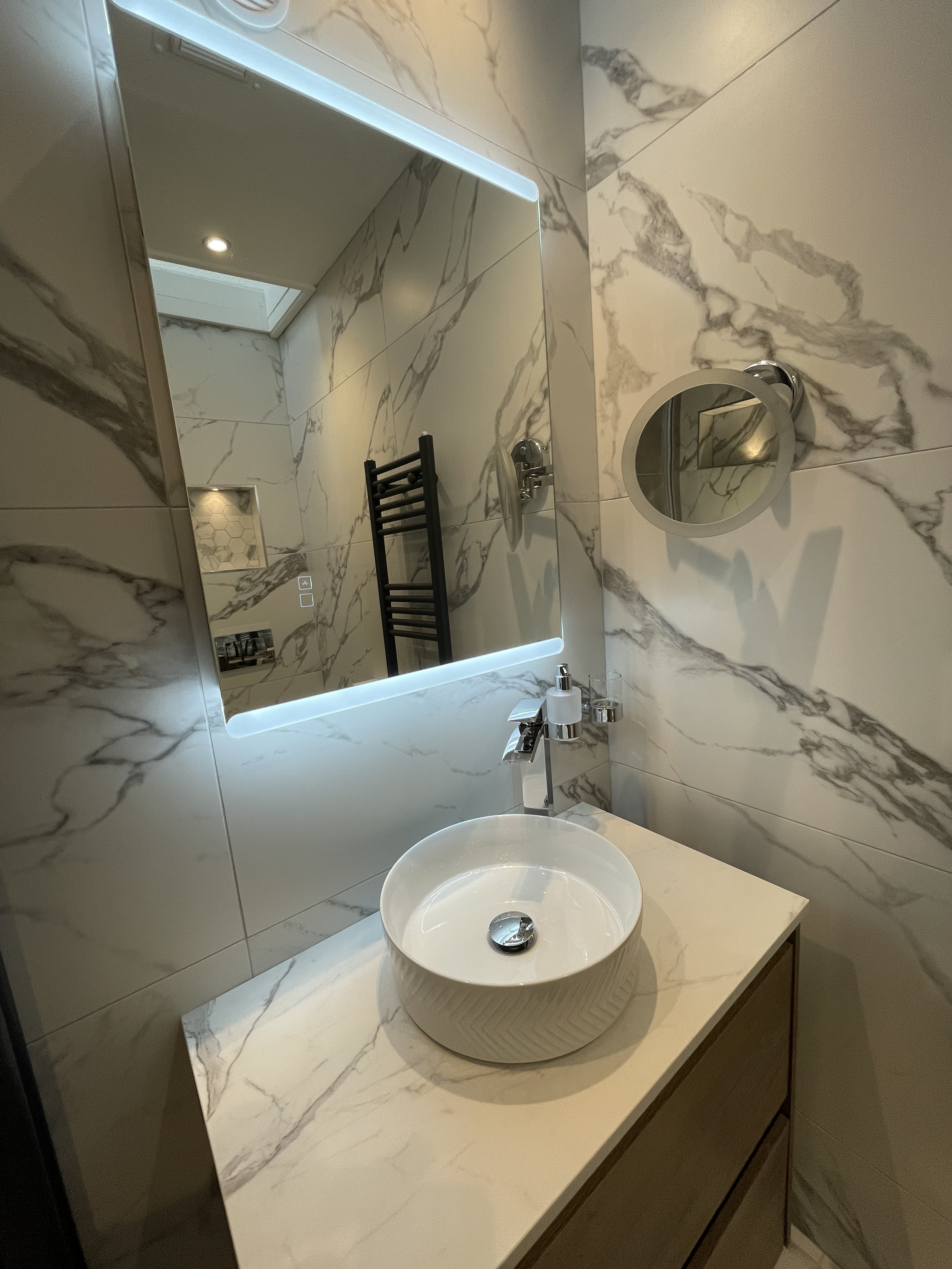 Tiled wall covering a circle sink and square backlit mirror