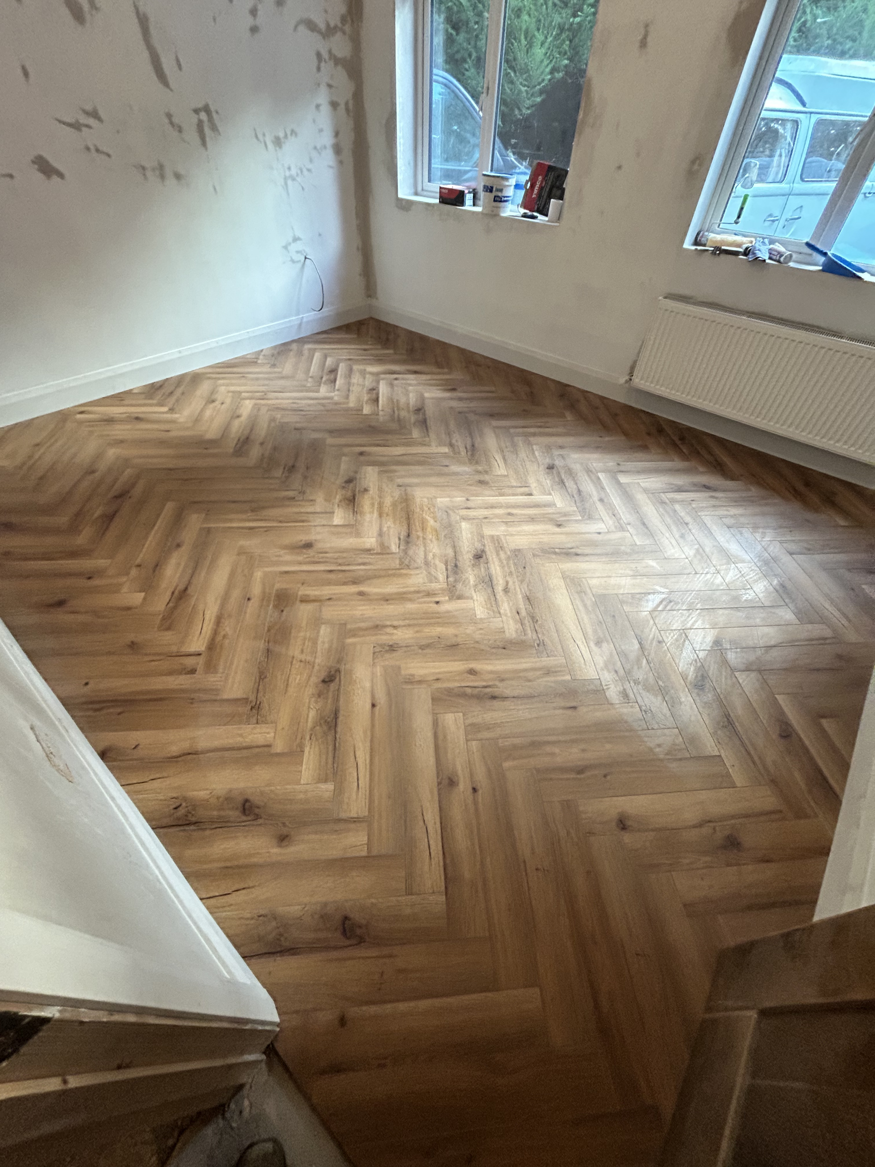Wooden herrinbone flooring in a square room with a window on the back wall